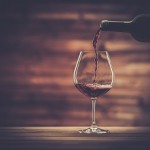 Pouring red wine into the glass against wooden background