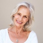 Close up portrait of beautiful older woman smiling and standing by wall