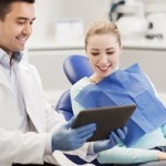 people, medicine, stomatology and health care concept - happy male dentist showing tablet pc computer to woman patient at dental clinic office