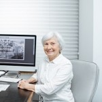 Portrait of a smiling senior woman sitting in the doctor's office with dental x-ray on the background