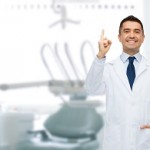 healthcare, profession, gesture, stomatology and medicine concept - smiling male middle aged dentist pointing finger up over medical office background