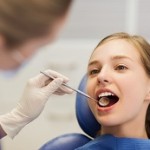 people, medicine, stomatology and health care concept - happy female dentist with mirror checking patient girl teeth up at dental clinic office